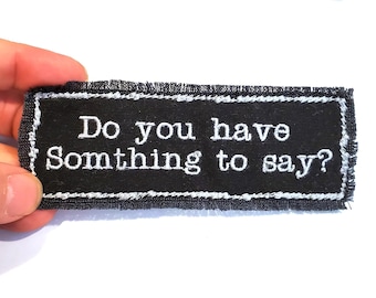 May include: Black fabric patch with white embroidered text that reads "Do you have something to say?"