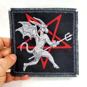 May include: A black patch with a red pentagram and a white embroidered image of a demon holding a trident. The demon has wings and is standing on a red pentagram.