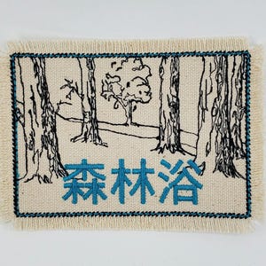 May include: A white fabric patch with black embroidered trees and a blue embroidered Japanese phrase "森 々 舎".