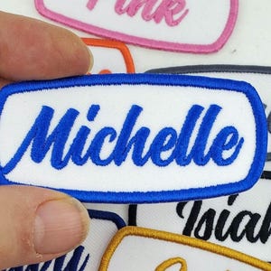 Puede incluir: Parche bordado azul con fondo blanco y el nombre "Michelle" en letras cursivas azules.