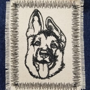 May include: A black and white embroidered patch of a German Shepherd dog's head with its tongue sticking out. The patch is on a white fabric background with a black stitched border.