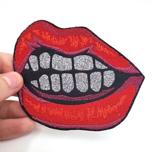 May include: Red embroidered patch of a mouth with white glitter teeth. The mouth is open in a wide grin.