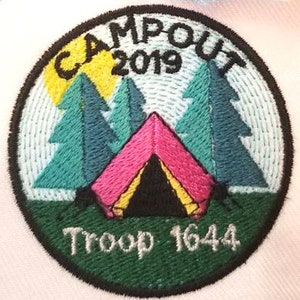 May include: A green and white embroidered patch with the text "Campout 2019" and "Troop 1644". The patch features a pink tent with a yellow and black interior, surrounded by three green trees and a yellow sun.