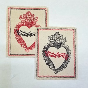 May include: Two embroidered patches with a stylized heart design. The heart is surrounded by a crown of thorns and flames. One patch is red and black, the other is black and white.