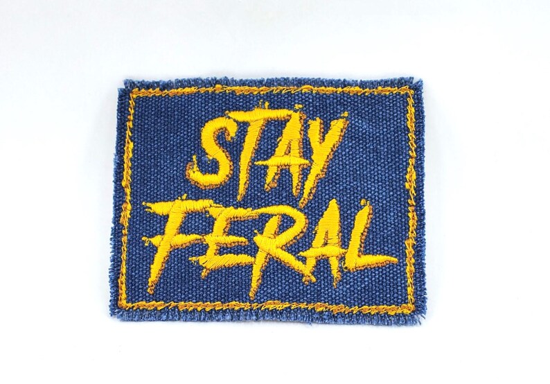 May include: A blue denim patch with yellow embroidered text that reads "Stay Feral".