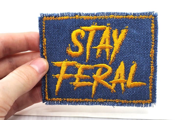 May include: A blue denim patch with yellow embroidered text that reads "Stay Feral".