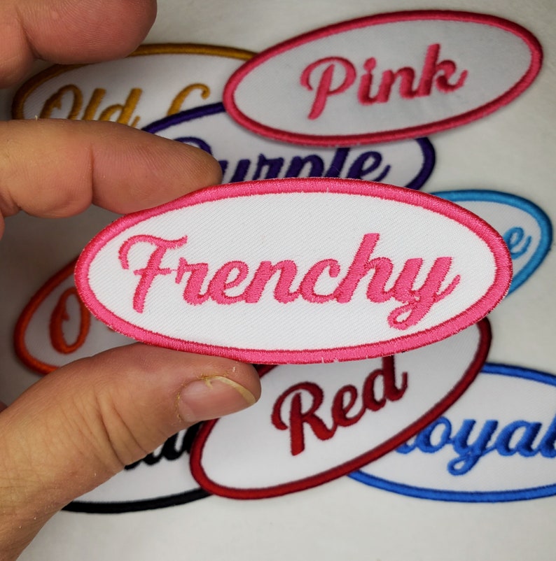 May include: A collection of white oval-shaped fabric patches with pink, red, blue, and orange embroidered lettering. The patches read "Pink", "Frenchy", "Red", "Loyal", and "Old Glory".