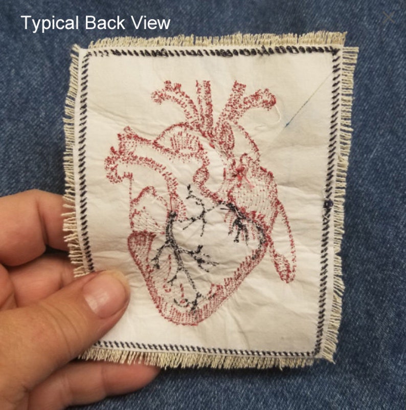 May include: A white fabric patch with a red embroidered anatomical heart design. The patch has a frayed edge and is surrounded by a black and white stitched border.