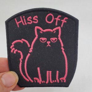 May include: Black iron-on patch with pink embroidered text that says "Hiss Off" and a pink outline of a cat with a grumpy expression.