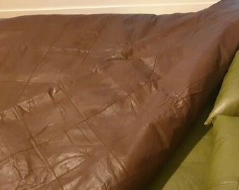 May include: A brown leather bedspread with a quilted pattern covers a bed with two green leather pillows. The pillows are also quilted.