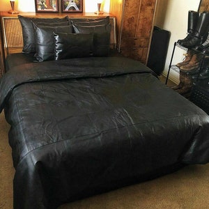 May include: A black leather bedspread with a quilted design. The bedspread is on a bed with black leather pillows.