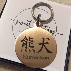 May include: A round copper keychain with a black engraved Japanese character and the text "Kuma-ken".