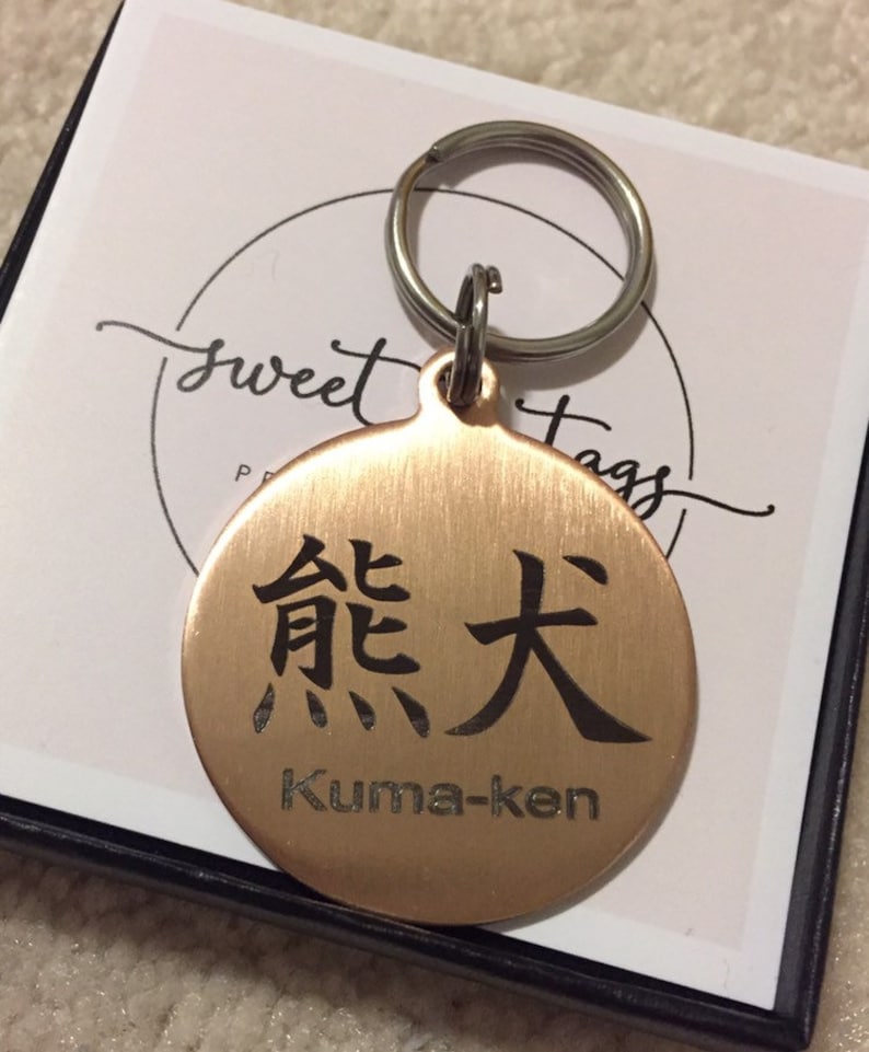 May include: A round copper keychain with a black engraved Japanese character and the text "Kuma-ken".