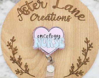 May include: Pink and blue glitter heart-shaped badge holder with the text "oncology NURSE". The badge holder is attached to a clear retractable badge reel with a sparkly silver charm.