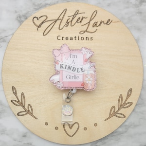 May include: Pink glitter badge reel with a pink and white picture frame with the text "I'm a Kindle Girlie" and a pink and white glitter drink with a flower on it.