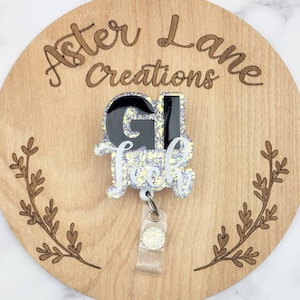 May include: A black and white glitter badge holder with the text "Gl Tech" on a wooden background with the text "Aster Lane Creations" engraved on it.