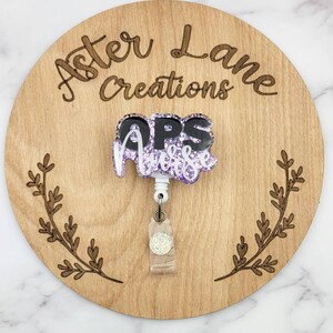 May include: Purple glitter and black "OPS Nurse" badge reel with a white retractable cord and a clear glitter charm.
