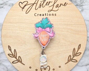 May include: A pink and green glitter carrot with a pink bow and the text "Happy Easter" on a wooden background. The carrot is attached to a retractable badge holder.