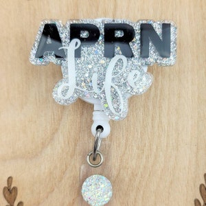 May include: A silver glitter badge reel with a black and white 'APRN Life' design. The reel has a clear plastic badge holder with a silver glitter circle.