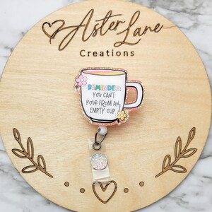 May include: A pink glitter coffee cup with the text "REMINDER: You can't pour from an empty cup."  The cup is attached to a clear badge reel with a glitter charm.