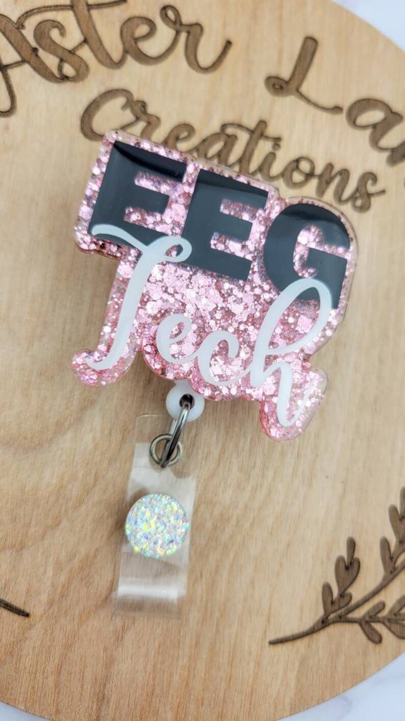 May include: Pink glitter resin badge holder with a black and white "EEG Tech" design. The badge holder has a clear plastic strap and a sparkly silver charm.