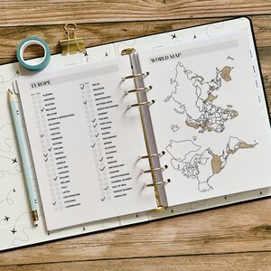 May include: Open planner with a world map and a Europe checklist. The pages are white with gold accents. A blue washi tape roll, a gold binder clip, and a light blue pencil are on the left side of the planner.