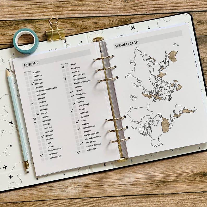 May include: Open planner with a world map and a Europe checklist. The pages are white with gold accents. A blue washi tape roll, a gold binder clip, and a light blue pencil are on the left side of the planner.