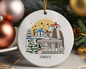 May include: White ceramic Christmas ornament featuring a colorful illustration of Greek landmarks, including a temple, church, and Acropolis. The word "GREECE" is printed at the bottom. The ornament has a gold string for hanging and is surrounded by Christmas decorations.