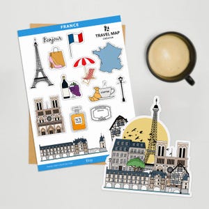 May include: A collection of France-themed stickers featuring iconic landmarks like the Eiffel Tower and Notre Dame Cathedral, along with French cultural elements such as a croissant, wine bottle, and the French flag. A cup of coffee sits nearby.