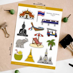 May include: A sheet of Thailand-themed stickers, 11.5cm x 16cm, featuring illustrations of a temple, flag, train, Buddha statue, boat, tuk-tuk, beach chair, palm tree, coconut, and pagoda. The text "THAILAND" and "TRAVEL JOURNAL COMPANY" are visible.