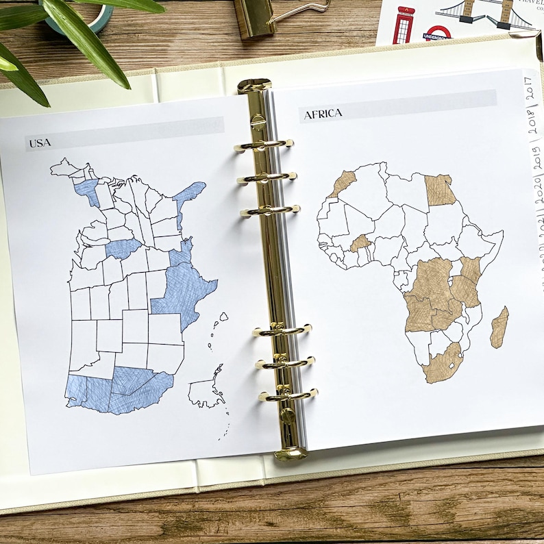 May include: Open planner with pages featuring hand-drawn maps of the USA and Africa. The USA map shows states colored in blue, while the African map highlights countries in brown. The planner is open to display the maps.