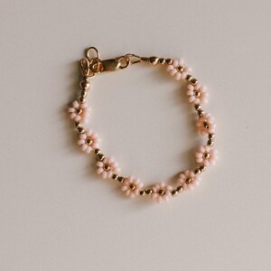 May include: A delicate gold bracelet featuring pink flower-shaped beads. The bracelet has a clasp fastening.