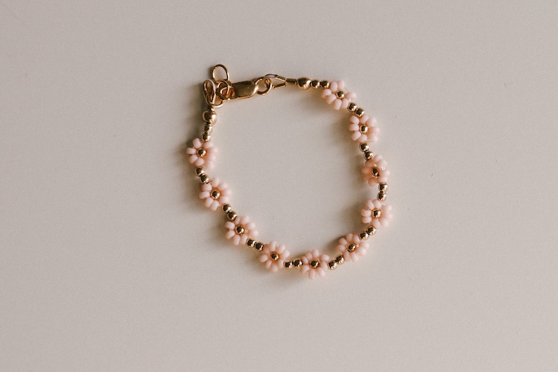 May include: A delicate gold bracelet featuring pink flower-shaped beads. The bracelet has a clasp fastening.