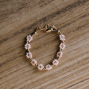 May include: A delicate gold bracelet with a chain and small pink flower-shaped beads.