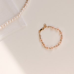 May include: A delicate gold bracelet with small pink flower accents. The bracelet is made of tiny gold beads and features a dainty clasp.