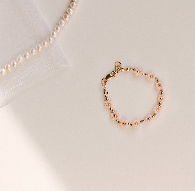 May include: A delicate gold bracelet with small pink flower accents. The bracelet is made of tiny gold beads and features a dainty clasp.