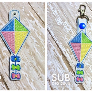 May include: A colourful kite-shaped key chain with a blue, green, pink, and yellow design. The kite has a string with three bows in blue, green, and pink.