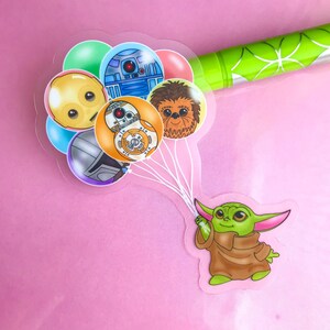 Puede incluir: Un personaje verde con orejas grandes sujetando cinco globos. Los globos son transparentes y presentan im&aacute;genes de dibujos animados de personajes de Star Wars, incluidos R2-D2, Chewbacca y C-3PO.
