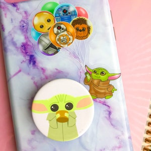 Puede incluir: Una funda de tel&eacute;fono de m&aacute;rmol morado y blanco con un pop socket que presenta un personaje verde con ojos grandes. El pop socket est&aacute; unido a la parte posterior de la funda del tel&eacute;fono. Tambi&eacute;n hay pegatinas en la funda del tel&eacute;fono de personajes de Star Wars.