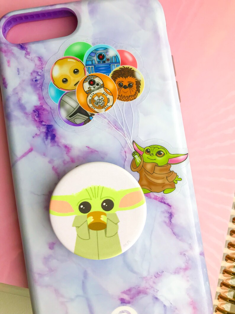 Puede incluir: Una funda de tel&eacute;fono de m&aacute;rmol morado y blanco con un pop socket que presenta un personaje verde con ojos grandes. El pop socket est&aacute; unido a la parte posterior de la funda del tel&eacute;fono. Tambi&eacute;n hay pegatinas en la funda del tel&eacute;fono de personajes de Star Wars.