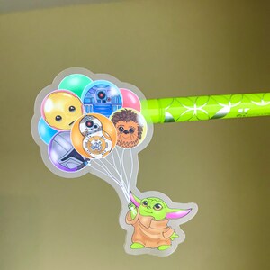 Puede incluir: Un personaje verde con orejas grandes sujetando un mont&oacute;n de globos. Los globos son transparentes y tienen im&aacute;genes de personajes de Star Wars, incluyendo R2-D2, Chewbacca y un droide amarillo.