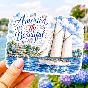 May include: A die-cut sticker featuring a white sailboat on blue water with a coastal house in the background. The text America The Beautiful is written in blue and red script, surrounded by small red and blue firework illustrations.