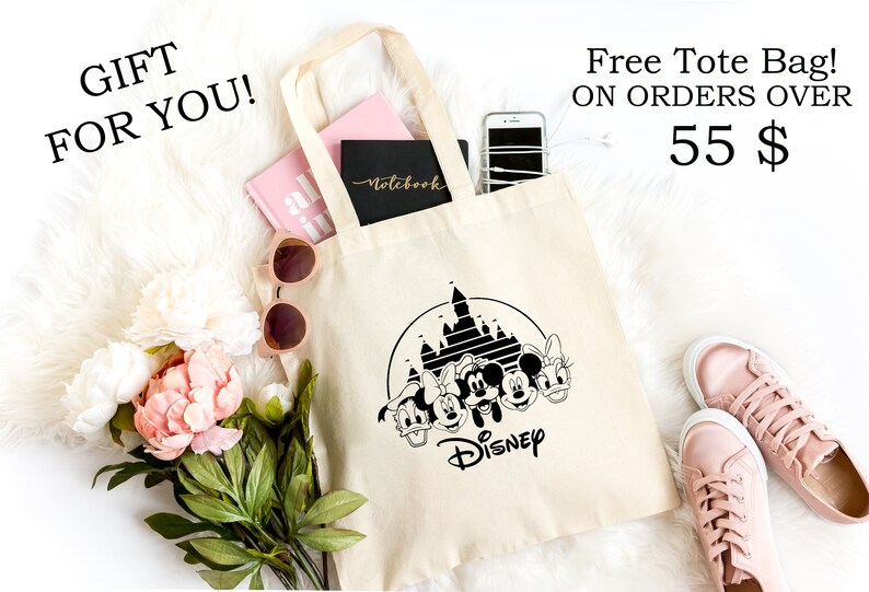 K&ouml;nnte beinhalten: Cremefarbene Tragetasche mit schwarzem Disney-Design, einschlie&szlig;lich Schloss und Figuren. Enth&auml;lt ein rosa Notizbuch, ein schwarzes Notizbuch und ein Smartphone. Der Text lautet "GIFT FOR YOU!" und "Free Tote Bag!" oben.