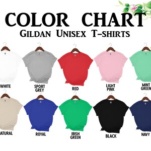 以下が含まれることがあります： GildanユニセックスTシャツの色見本。白、スポーツグレー、赤、ライトピンク、ミントグリーン、ナチュラル、ロイヤルブルー、アイリッシュグリーン、黒、ネイビーなど、さまざまな色があります。各シャツはハンガーに掛けられています。