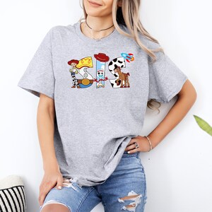 May include: Gray t-shirt with a graphic of the characters from the Toy Story movie. The graphic spells out the word "SIS" with each letter represented by a different character.
