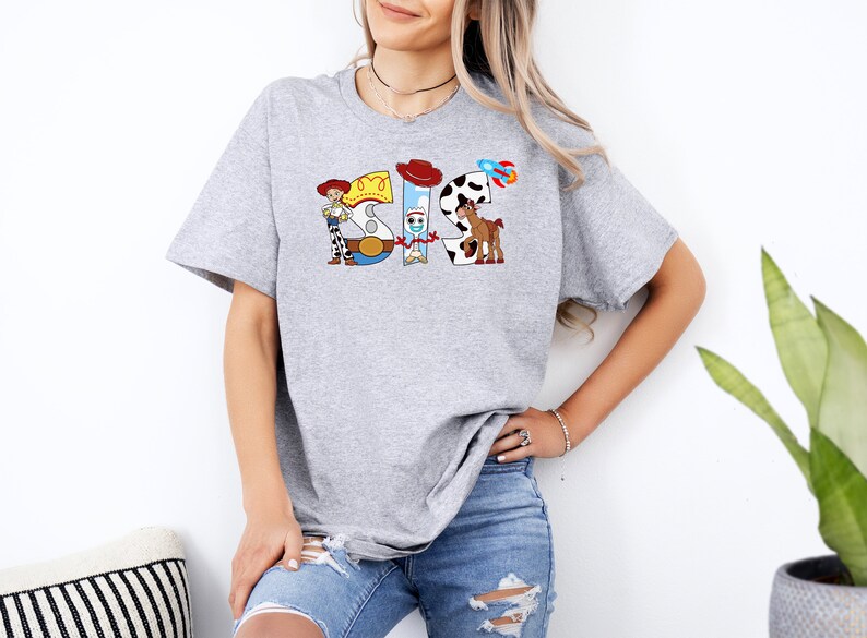 May include: Gray t-shirt with a graphic of the characters from the Toy Story movie. The graphic spells out the word "SIS" with each letter represented by a different character.