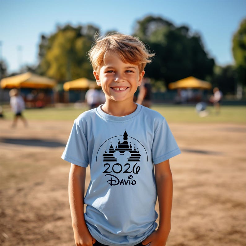 K&ouml;nnte beinhalten: Hellblaues T-Shirt mit schwarzem Schloss-Grafik und dem Text "2026 David". Das T-Shirt besteht aus einem weichen Material. Das T-Shirt wird von einem l&auml;chelnden Kind getragen. Geeignet f&uuml;r den t&auml;glichen Gebrauch.
