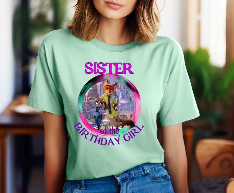 以下が含まれることがあります： Zootopiaのキャラクターのカラフルなグラフィックと「SISTER of the BIRTHAY GIRL」の文字が円でデザインされた、薄い緑色のTシャツ。半袖でクルーネックです。