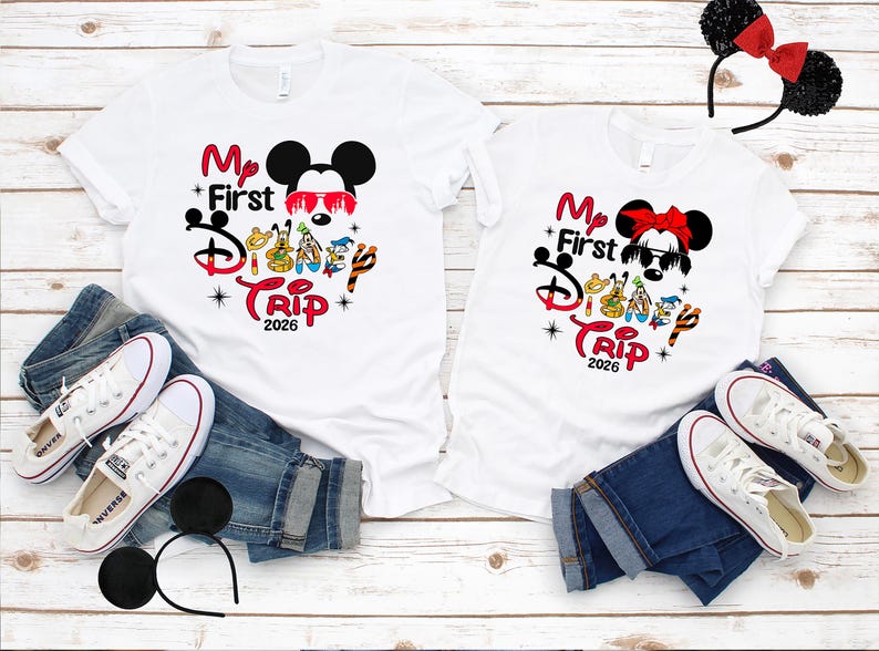 Puede incluir: Dos camisetas blancas con el texto "My First Disney Trip 2026" y gr&aacute;ficos de Mickey y Minnie Mouse. Las camisetas se combinan con vaqueros azules, zapatillas blancas y diademas con orejas de rat&oacute;n. La imagen est&aacute; sobre una superficie de madera clara.