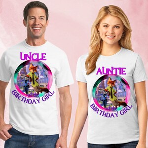 以下が含まれることがあります： ズートピアのキャラクターが描かれたカラフルなグラフィックの白いTシャツ。片方のシャツには紫色の文字で「UNCLE of the BIRTHDAY GIRL」、もう片方には「AUNTIE of the BIRTHDAY GIRL」と書かれています。男性と女性が着用しています。